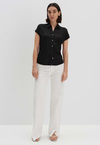 Camicia nera a maniche corte con bottoni e colletto, abbinata a pantaloni bianchi a gamba larga. L'outfit presenta texture lisce e un design ordinato.