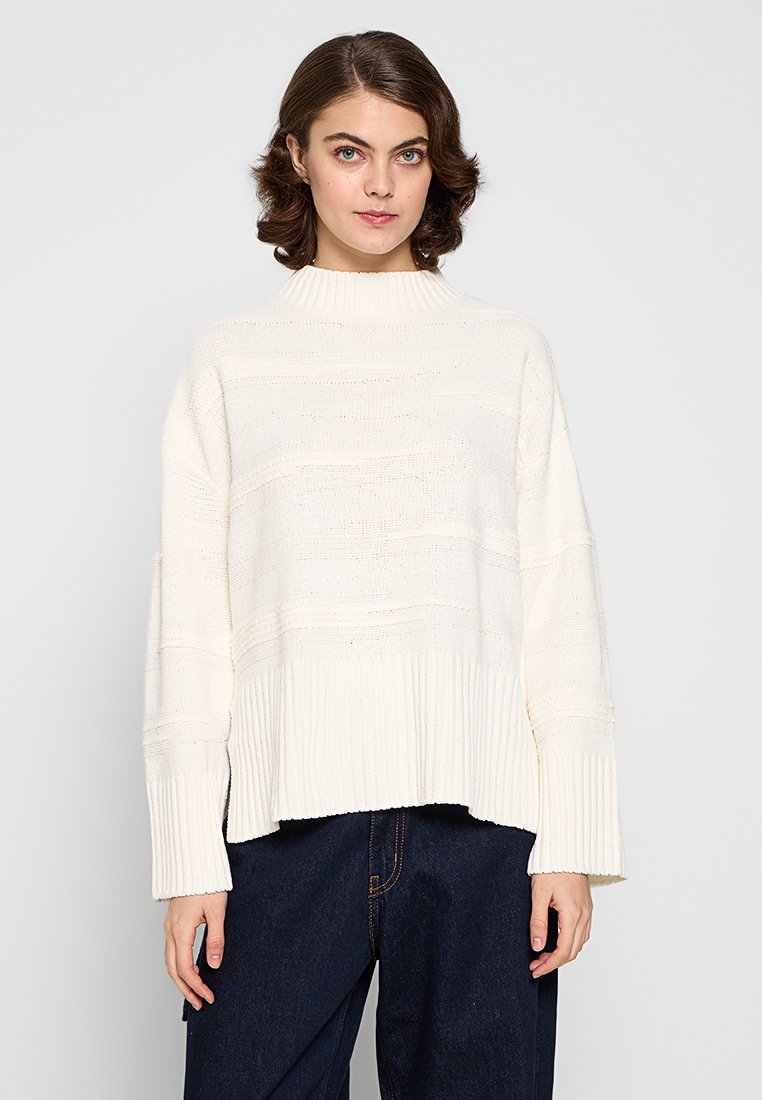 Suéter de punto grueso en blanco roto. Presenta un cuello alto, corte suelto, dobladillo y puños acanalados, con rayas horizontales texturizadas.