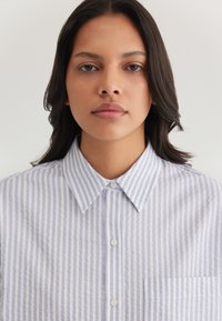 Blue and white vertically striped button-up shirt with a collar and a chest pocket; fabric appears lightweight and textured.