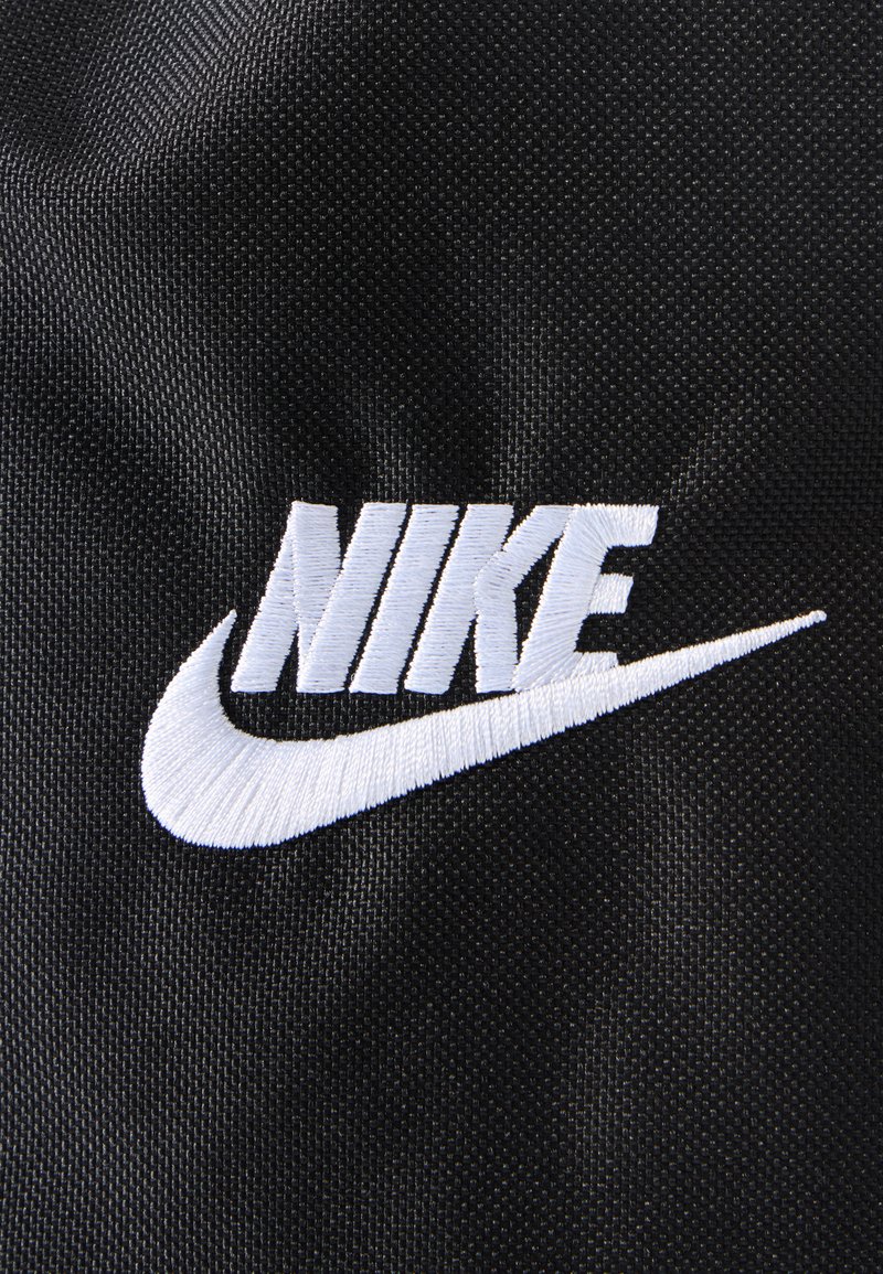 White embroidered Nike logo with swoosh on textured black fabric background.