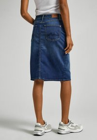 Tummansinisestä denimhameesta, polven pituinen, jossa on kaksi takataskua ompeluyksityiskohdilla. Yhdistetty vaaleanharmaisiin lenkkareihin.