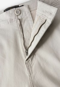 Beige pamut nadrág elülső cipzárral és gombos záródással. Erősített varrás jellemzi, sima tapintású. A cipzár ezüstszínű fém.