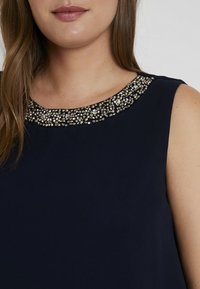 Marinblå ärmlös klänning med en utsmyckad halsringning prydd med klara rhinestones och en slät textur, designad för en figurpassande siluett.