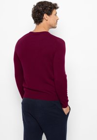 Bordeauxrode trui met een ronde hals, lange mouwen en een aansluitende zoom, gemaakt van een zachte stof. Gecombineerd met marineblauwe broek met achterzakken.