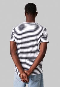 T-shirt in cotone a maniche corte con righe orizzontali blu navy e bianche, girocollo e vestibilità comoda, abbinato a jeans di denim azzurri.