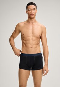 Černé boxerky s námořnickým pasem, které mají těsně padnoucí střih, hladkou texturu a kontrastní prošívání. Model je bez trička.