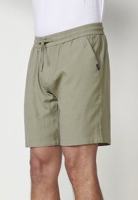 Khaki šortai, pagaminti iš lengvos medžiagos, su elastinga juosta ir raišteliu, turintys šoninius kišenes ir švarius siuvimo detalus.