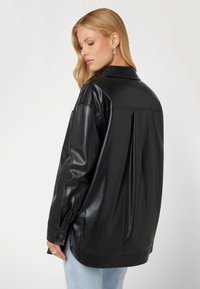 Giacca camicia in pelle nera con vestibilità rilassata, colletto a punta, polsini con bottone e una piega sul retro per una maggiore struttura. Texture liscia e lucida.