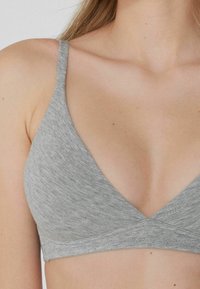 Grijze driehoek bralette met dunne banden, textuurstof en een diepe V-halslijn. Minimalistisch ontwerp zonder zichtbare hardware of versieringen.