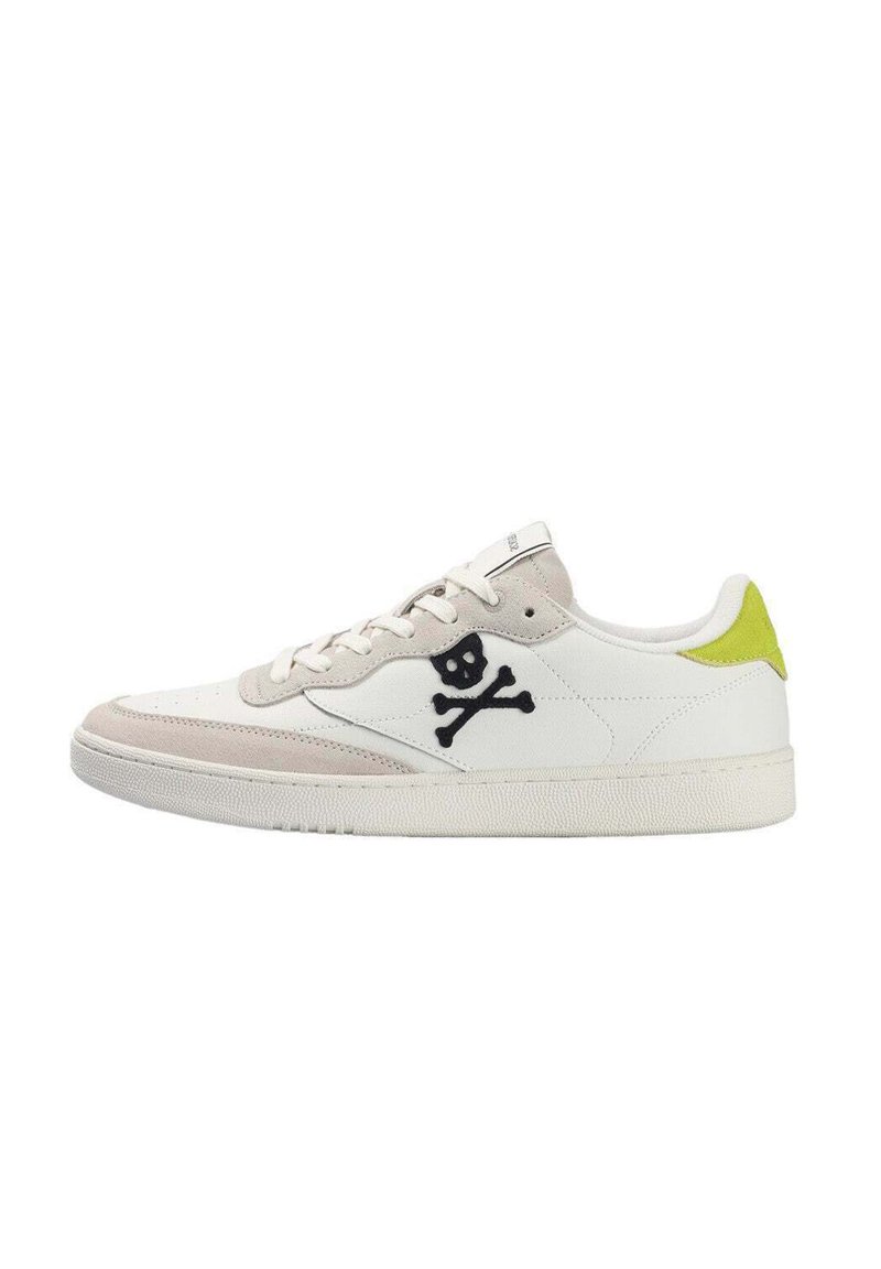 Zapatilla blanca de corte bajo con acentos de ante beige, logo de calavera y tibias negras en el lateral, y detalle amarillo brillante en el talón.