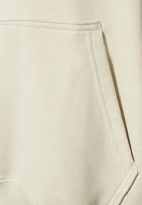 Felpa color crema con tasca frontale, tessuto morbido, cuciture a contrasto e design dal taglio rilassato.