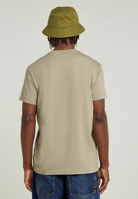 Beige t-shirt met korte mouwen en een ronde hals, met een gladde textuur en een relaxed fit, gecombineerd met een groene bucket hat.