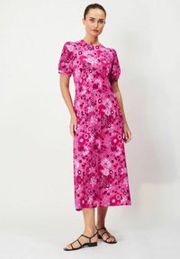 Vaaleanpunainen kukkakuvioinen midi-mekko, jossa on lyhyet puffihihat, esittelee eloisaa kukkakuviota ja geometrisia muotoja. Yhdistetty mustien hihnallisten sandaalien kanssa.