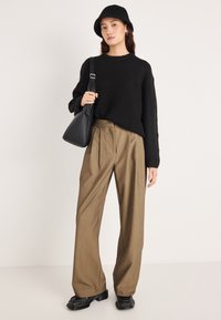 Μαύρο πλεκτό πουλόβερ, καφέ παντελόνι με φαρδιά μπατζάκια, μαύρο καπέλο τύπου bucket και μαύρη τσάντα ώμου. Λείο ύφασμα, εφαρμοστή γραμμή και casual σχεδιασμός.