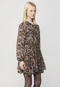 Zwarte jurk met een paisleypatroon in bruin, blauw en roze. Heeft een knoopsluiting aan de voorkant, lange mouwen en een rucheszoom. Gladde stoftextuur.