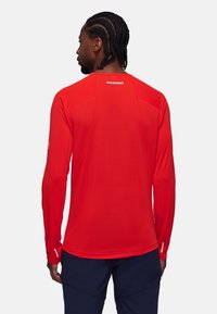 Camisetta rossa a maniche lunghe in tessuto leggero, con collo tondo, logo discreto sulla schiena e vestibilità atletica. Mostra un dettaglio di cucitura.