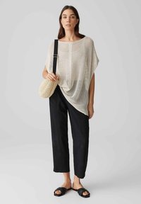 Haut en tricot beige clair, ample avec des manches larges, associé à un pantalon noir à coupe droite et des sandales plates noires ; sac rond en osier.