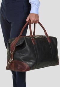 Black leather duffel bag with brown leather accents, featuring double handles, a zipper closure, and metal hardware details.
