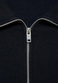 Jachetă bleumarin cu fermoar, dintr-un material texturat, având un fermoar metalic și accesorii argintii. Designul prezintă un prim-plan al gâtului și detalii ale fermoarului.
