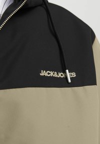 Crna i bež dukserica s patentnim zatvaranjem, teksturiranom tkaninom, podesivom vrpcom i istaknutim логом "JACK&JONES".