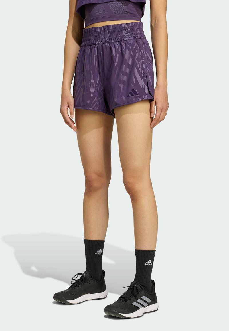 Lila Sportshorts mit strukturiertem Muster und elastischem Bund, kombiniert mit schwarzen Schuhen und Kniestrümpfen.