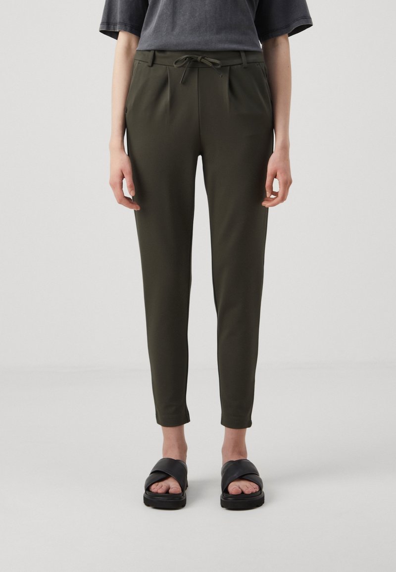 Pantalons ajustés vert olive avec une taille à cordon de serrage, dotés de plis et d'un design fuselé. Associés à des sandales noires plates.