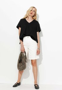 T-shirt noir en coton en V, coupe ample, associé à un short blanc à mi-cuisse et un sac à imprimé léopard. Des ballerines noires ornées complètent le look.