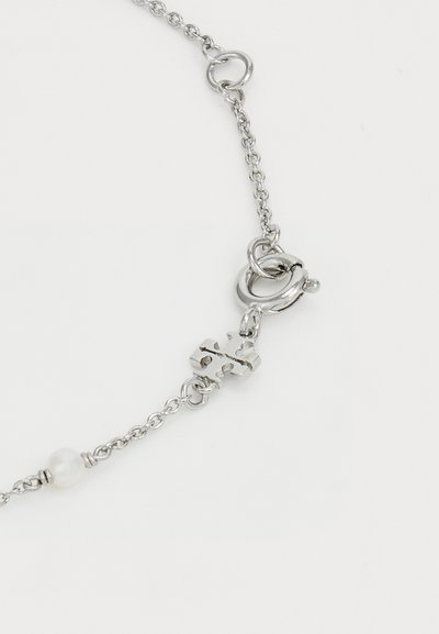 Pulsera de cadena de plata con cierre de tipo toggle, una pequeña perla blanca y un detalle metálico en forma de "X".