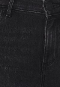 Svarta denimjeans med en slät yta, med en framtida ficka, synliga sömmar och en svart metallknappknäppning.