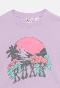 Πουκάμισο λιλά με υφή, με γραφικό ενός ροζ ήλιου, γκρίζων βουνών, φοίνικα, τροπικών λουλουδιών και κείμενο "ROXY" σε διακοσμητική γραμματοσειρά.