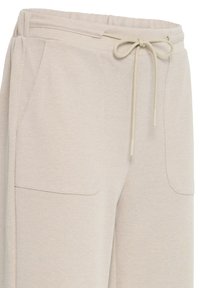 Pantalon de survêtement beige texturé avec taille élastique, cordon de serrage et poches plaquées à l'avant.