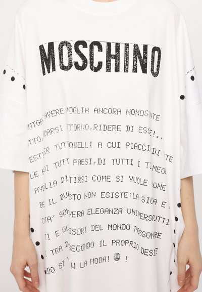 Fehér, oversized póló fekete "Moschino" logóval, grafikus szövegnyomattal és pöttyös díszítéssel a ujjakon. Puha anyag, laza fazon.