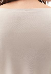 Hellbeige Oberteil mit einer glatten, weichen Textur und einem weit ausgeschnittenen, schulterfreien Ausschnitt. Nahtdetails sind dezent entlang des Randes sichtbar.
