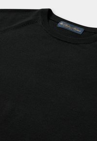 Maglione nero girocollo con trama a maglia fine e un'etichetta blu navy con scritta dorata cucita all'interno del colletto.