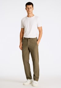 Camiseta blanca de cuello redondo combinada con pantalones verdes oliva con cintura ajustable. El modelo lleva zapatillas blancas. Atuendo sencillo y casual.