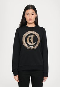 Schwarzer Pullover mit langen Ärmeln, der auf der Vorderseite ein runden Logo-Design in Gold und Schwarz aufweist. Gerippte Bündchen und Saum, glatte Stoffoberfläche.