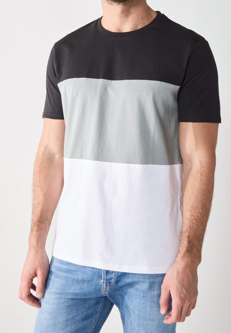 T-shirt noir, gris et blanc avec un motif à blocs de couleurs horizontaux. En coton, col ras du cou, manches courtes, et texture lisse.