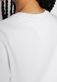 White sweatshirt with a subtle V-shaped seam at the back neckline. Smooth texture, ribbed collar, and soft fabric visible.