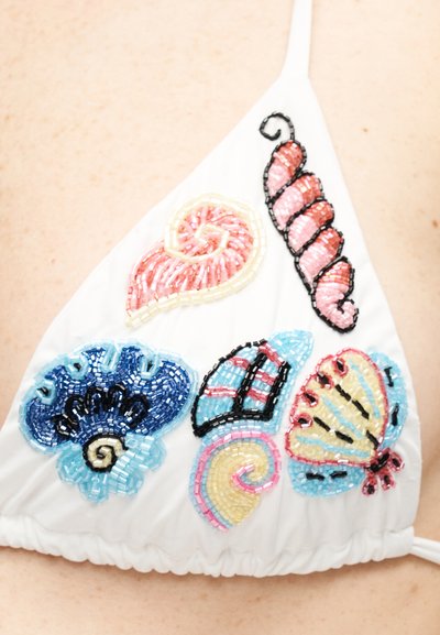 Tissu blanc orné de motifs colorés de coquillages et de papillons en perles, comprenant des perles roses, bleues, jaunes et noires disposées en motifs.