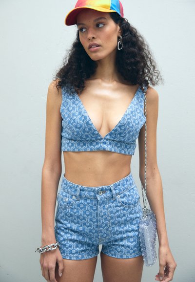 Blå denim crop top og shorts med et mønstret design, der har en dyb V-halsudskæring, samt en klar akryl skuldertaske med kædestrop.