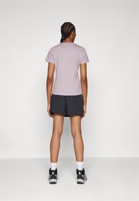 Tričko s krátkým rukávem v levandulové barvě spárované s tmavými šortkami. Tento outfit má ležérní střih, hladkou texturu a běžný střih.