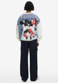 Il denim e la felpa bianca presentano una grafica colorata di Topolino e Minni Mouse sulla schiena, con la scritta "Insieme" ricamata sopra.