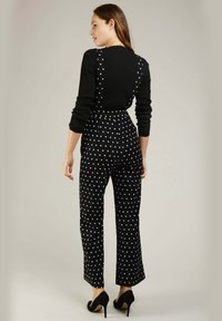 Top noir à manches longues côtelé associé à une salopette à pois en tissu doux ; taille ajustée avec une coupe large, mise en valeur par des talons hauts.