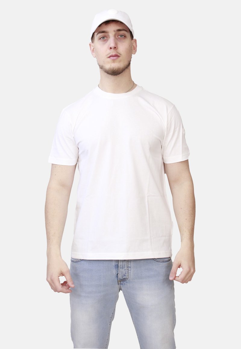 T-shirt bianca in cotone con maniche corte, scollatura rotonda e spalle senza cuciture, abbinata a jeans blu chiaro e un cappellino bianco.