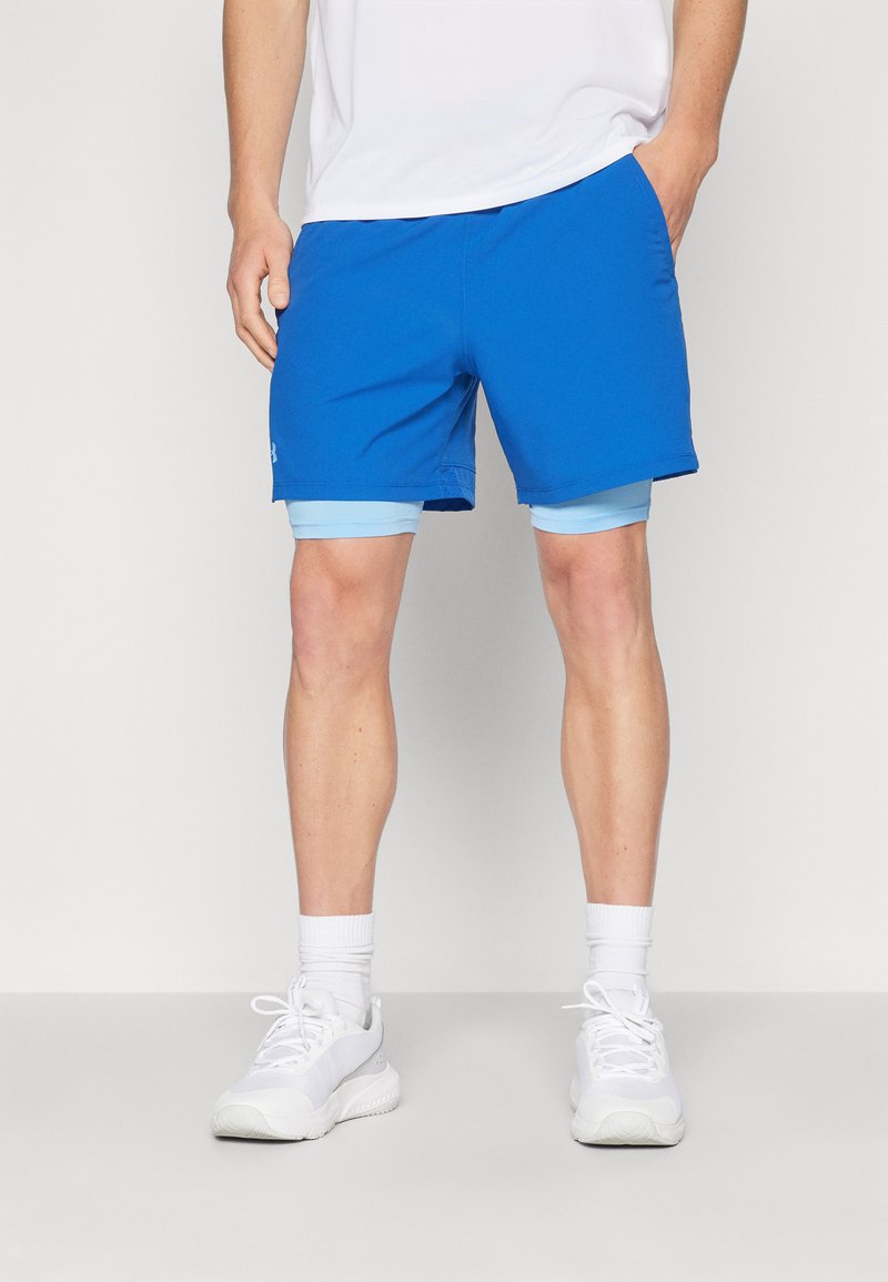 Pantalones cortos deportivos azules con una textura suave, que presentan un forro interior de color azul claro. Llevado con zapatillas blancas y calcetas de longitud media.