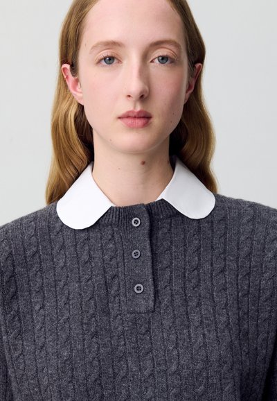 Maglione grigio lavorato a maglia con motivo a trecce, dotato di un collo bianco e una patta con tre bottoni. Texture morbida, design casual.