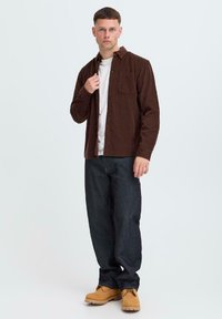 Brown corduroy shirt over a white t-shirt, paired with dark denim jeans and tan boots. Simple design, regular fit, casual style.