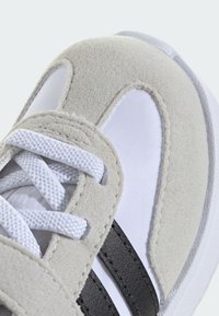 Šedé semišové a biele sieťové športové topánky s čiernymi pruhmi. Obsahujú biele šnúrky a polstrovaný golier. Hladký povrch s prešívanými detailmi.