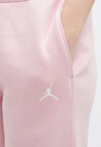 Zbliżenie na biodro osoby w różowych spodniach z białym logo Jumpman, z ręką częściowo w kieszeni.