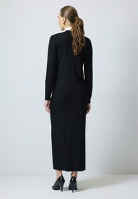 Čierny rebrovaný pletený sveter a dlhá sukňa, s dlhými rukávmi a priliehavým strihom. Zvýraznené ostrými podpätkami, elegantné a jednoduché.
